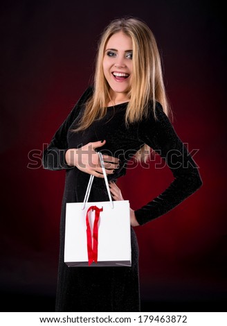 Young woman in black dress with shopping bag on a dark red background