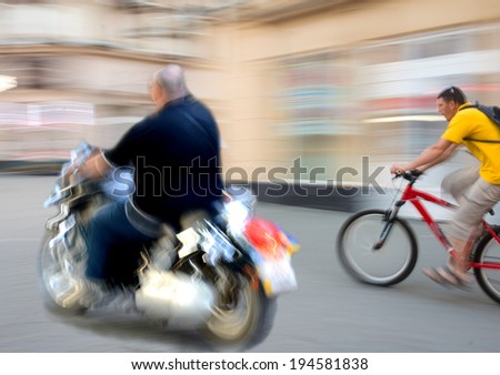 Motorcyclist and cyclist in motion going down the street . Intentional motion blur