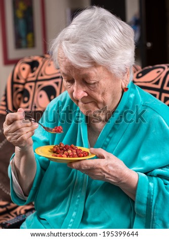 Old woman eating strawberry at home