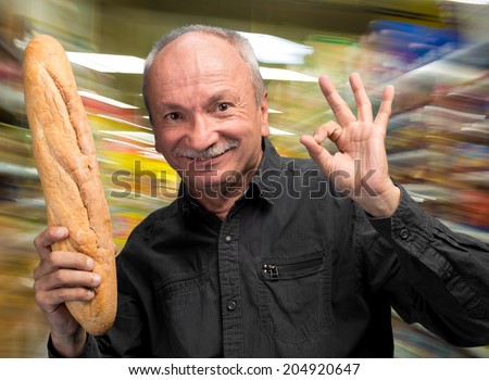 Happy senior man holding fresh baguette in supermarket