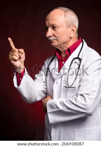 Senior doctor pointing upwards on a dark red background