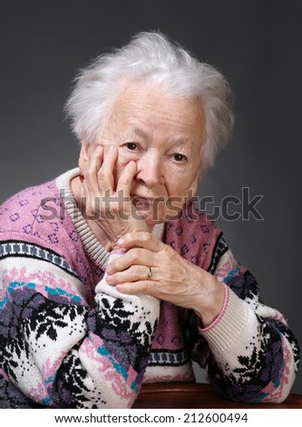 Portrait of old sad woman on a gray background