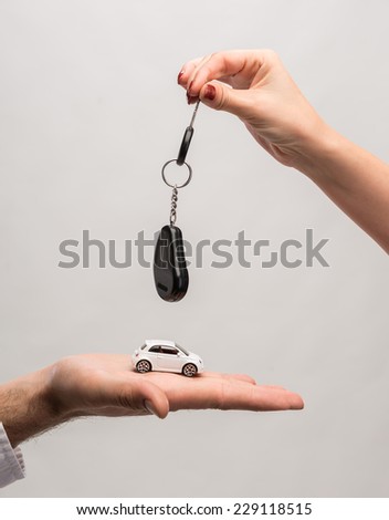 Man holding small car, woman holding car key on a gray background