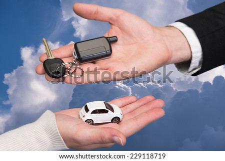 Man holding small car key, woman holding small car against sky