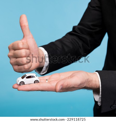 Closeup of  businessman in  black suit holding small car model and showing ok sign