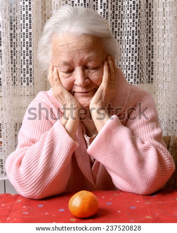 Old woman looking at tangerine at home