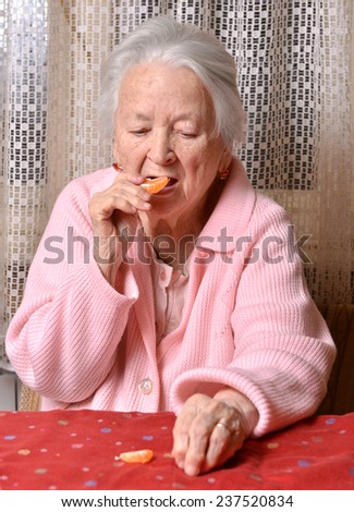 Old woman eating tangerine at home