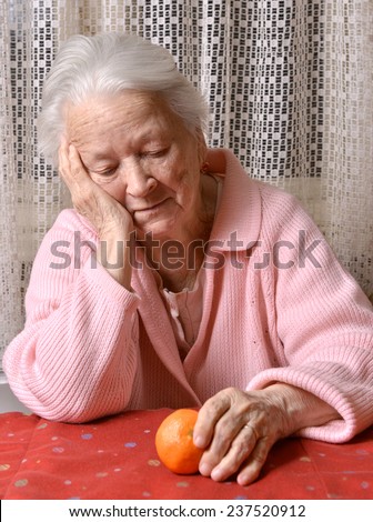 Old woman looking at tangerine at home