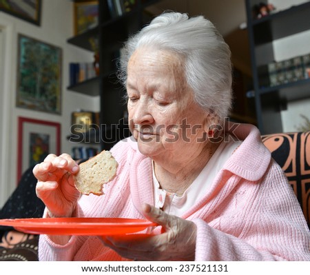 Old woman eating a slice of  bread at home