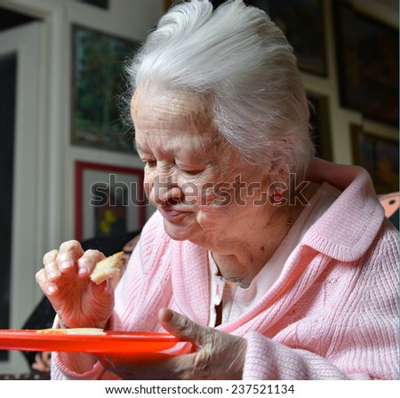 Old woman eating a slice of  bread at home