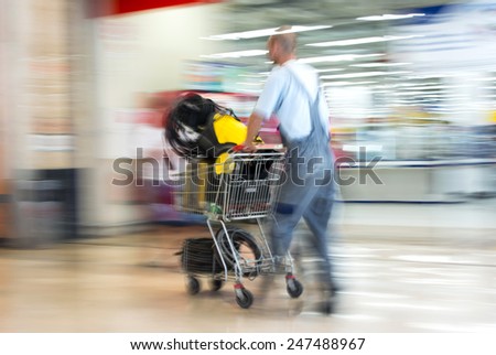 Worker in overalls pushing trolley in hardware shop. Intentional motion blur