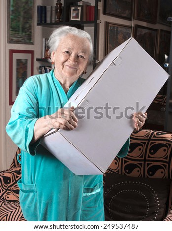 Happy old woman holding a large cardboard box at home