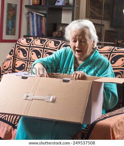 Happy old woman holding a large cardboard box at home
