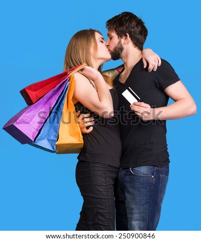 Happy kissing couple with shopping bags on a blue background. Man holding credit card