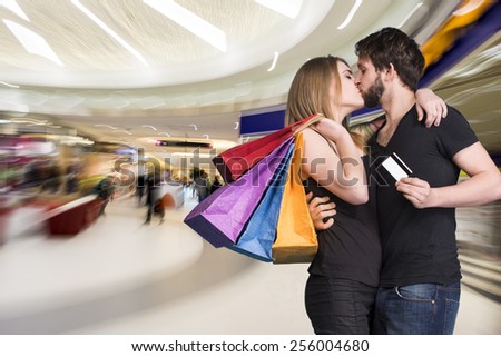 Happy kissing couple with shopping bags in the mall. Man holding credit card