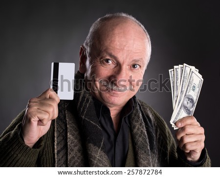 Lucky elderly man holding dollar bills and credit card on a dark background