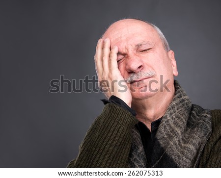 Pain, headache. Elderly man covers his face with hand