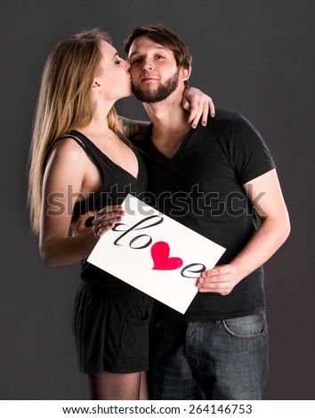 Happy couple holding board with declaration of love on a dark background