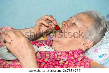 Old sick woman eating strawberry at home