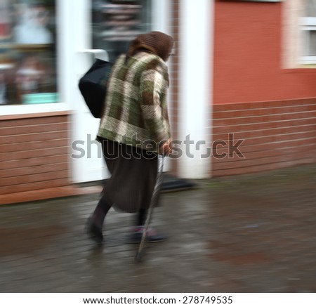 Old woman walking with a cane on a city cane. Intentional motion blur