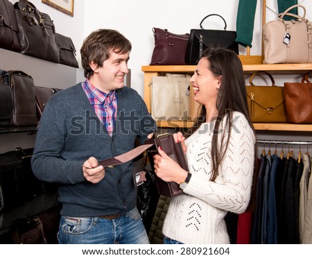 Shop assistant showing leather bag to beautiful woman at the mall