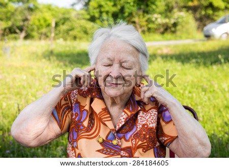 Old woman  covers her ears with fingers. Suffering from a loud sound.