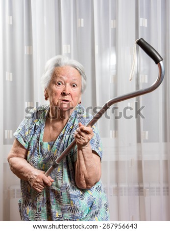 Old angry woman threatening with a cane at home