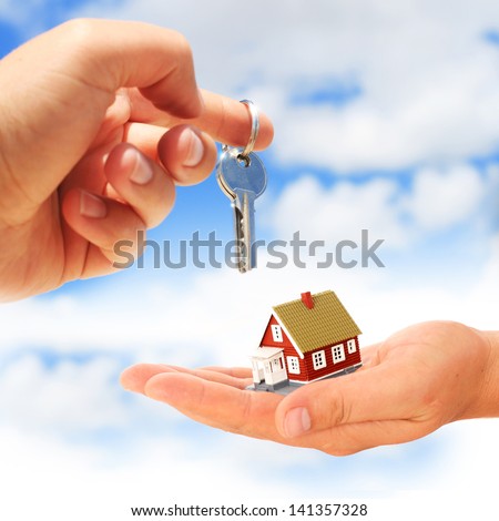 Key in hand and house over sky.