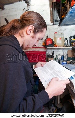 A man reads instructions before commencing maintenance work on a car in his garage