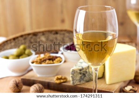 White Wine, cheese, nuts, olives, dried fruit, bread and garlic on wooden table