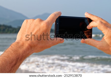 Man\'s hand holding phone horizontaly against the background of sea and mountains