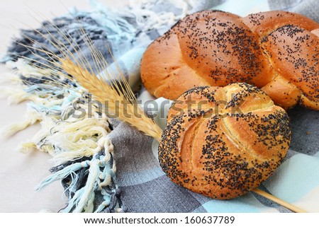 Kaiser roll with poppy seeds and braided poppy seed bread on a table cloth.