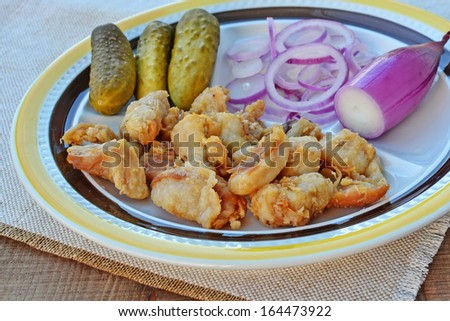 Fried pieces of pork greaves with red torpedo onions and pickles.
