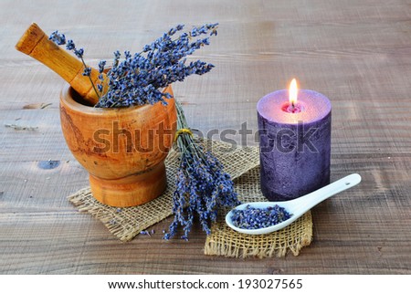 Wooden mortar with dried lavender flowers and scented candle on wooden background.
