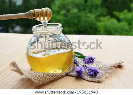 Jar of herbal honey and wooden deeper with fresh flower.