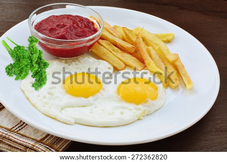 Sunny side up with french fries and ketchup on white plate over wooden table.