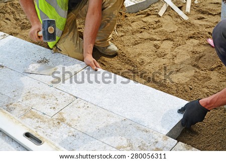 Worker tapping paver into place with rubber mallet. Installation of granite paver blocks series with motion blur on hammers and hands.