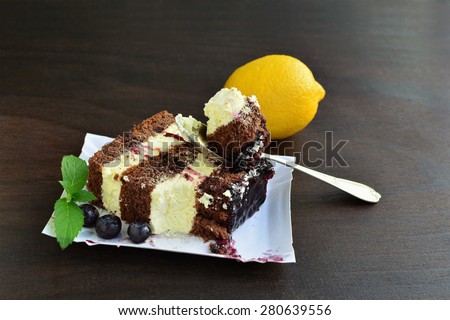 Sponge cake with lemon icing and blueberry sauce on paper tray over dark background.