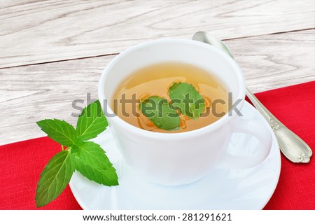Cup of mint tea with mint leaves on red table cloth over wooden table.