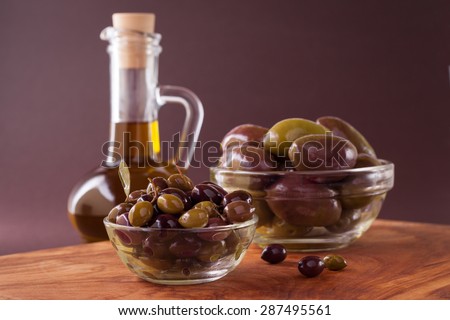 Great olives and small olives in glass cup on the olive wood board on a apricot background