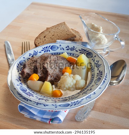 Boiled beef Tafelspitz soup broth with potato, carrot, cauliflower, kohlrabi, bred and horseradish sauce in glass sauce boat with cutlery and napkin on the wood table. Germany traditional cuisine