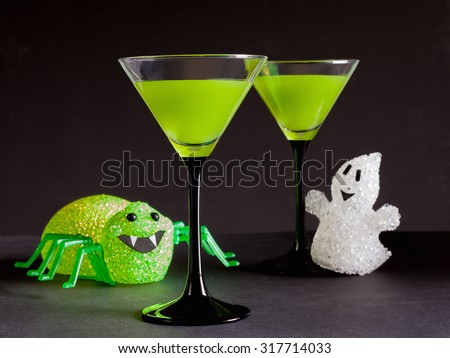 Toxic Green cucumber cocktail for Halloween in a cocktail glass with a green glowing spider and white ghost on the black background