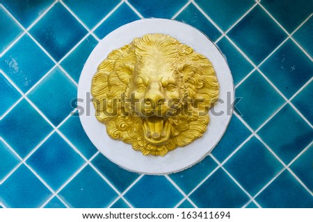 Golden statue of a lion head on a blue tiles wall