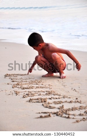 The boy is writing  art word on the sand of beach