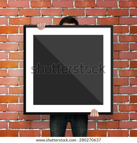 man holding poster mockup template with black frame on brick bac