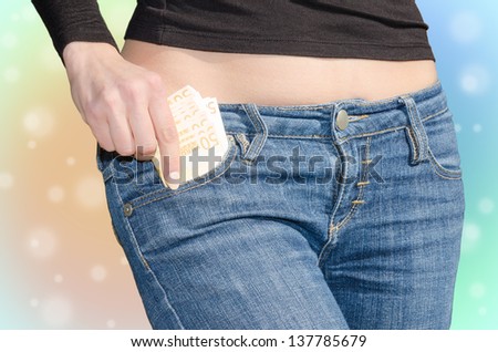 Young woman with naked tummy puts money in your jeans pocket on colored background