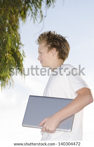 Youngster with notebook stands in nature under tree in profile