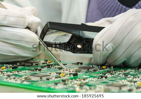 Woman in antistatic gloves holding pincette and magnifier repairing electronic components on PCB