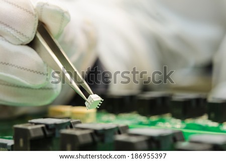 Female hand in ESD gloves holding tweezers and assembling white microchip on printed circuit board