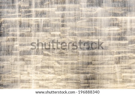 Falling water stream against stone wall rough texture with night backlight